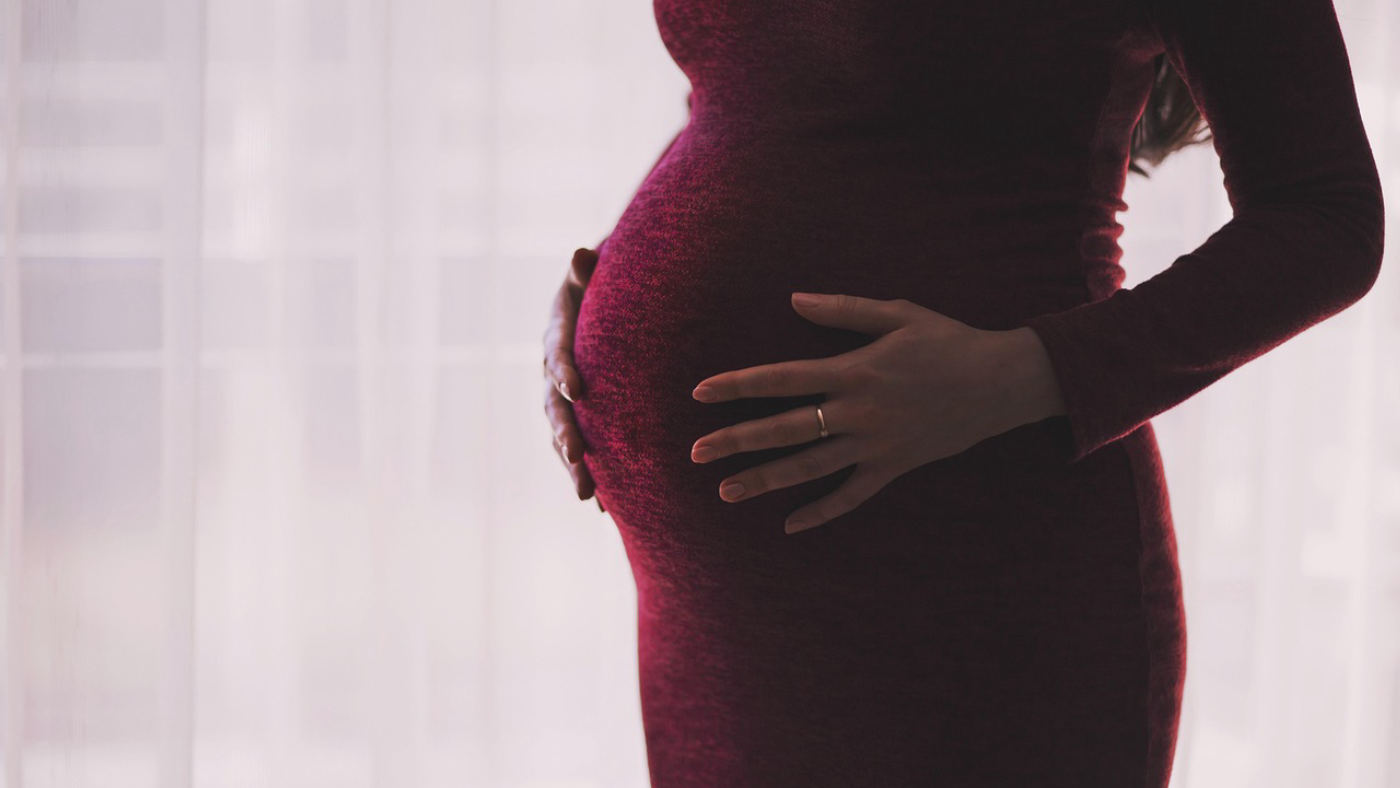 孕婦在窗邊的柔和光線中安靜地站著，手放在肚子上