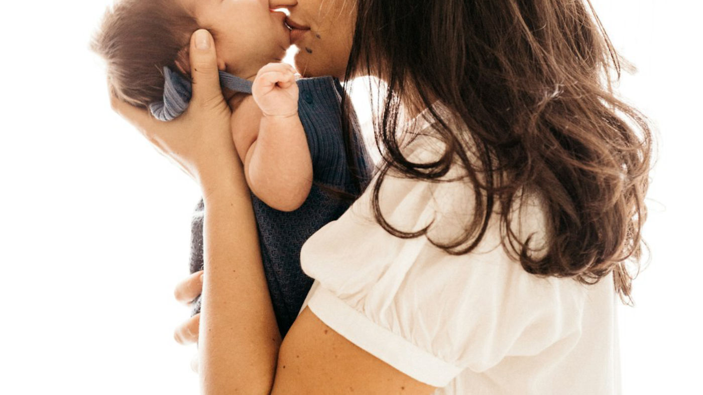 A mother holding her newborn close, her face turned towards the baby.