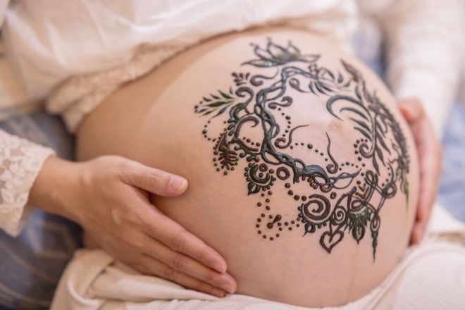 孕婦的肚子上畫著海娜圖騰，一雙手輕輕放著