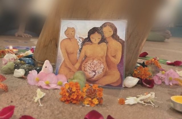 女人圈祭壇上，畫著女人們圍著孕婦的畫卡，周圍是花和燭光